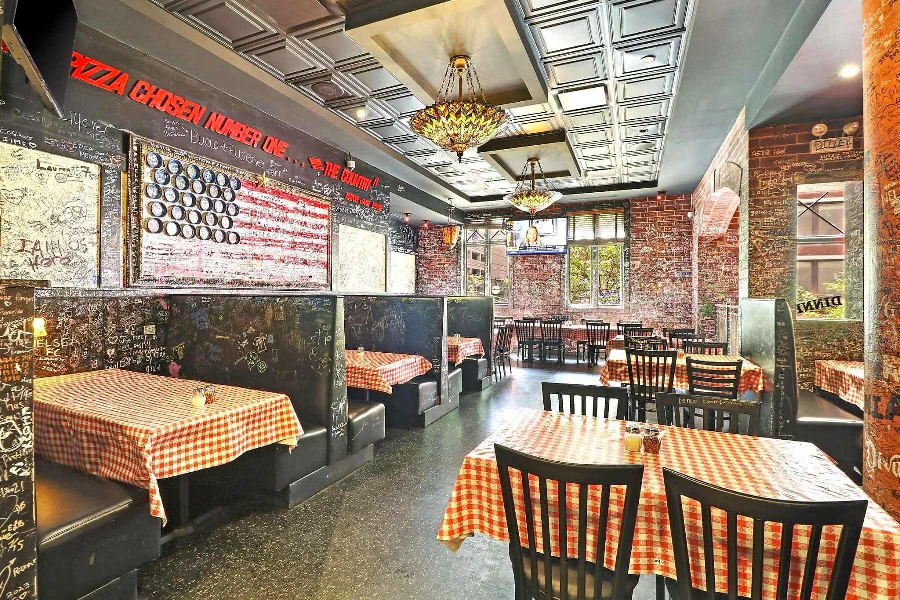 Graffiti-covered dining room at Gino's East Magnificent Mile, with a wall-mounted TV and red-checkered tablecloths