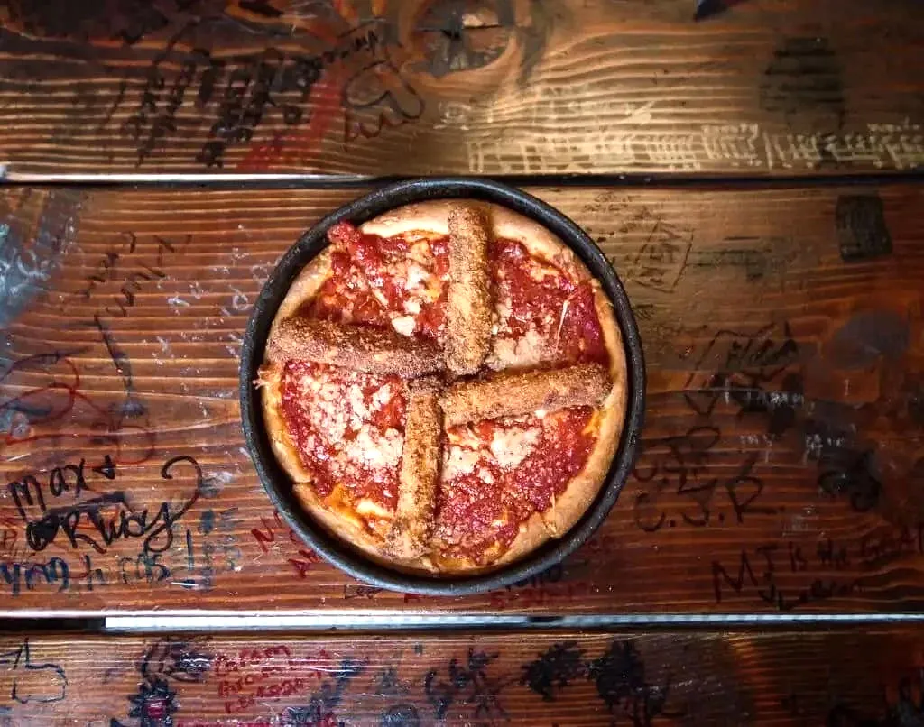 Deep-dish pepperoni pizza in cast iron pan on wooden table with graffiti