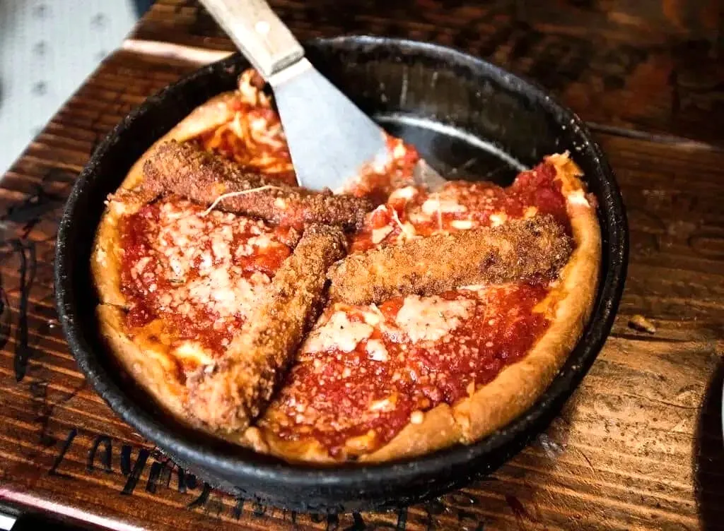 Cast iron skillet with two slices of pepperoni deep-dish pizza and server