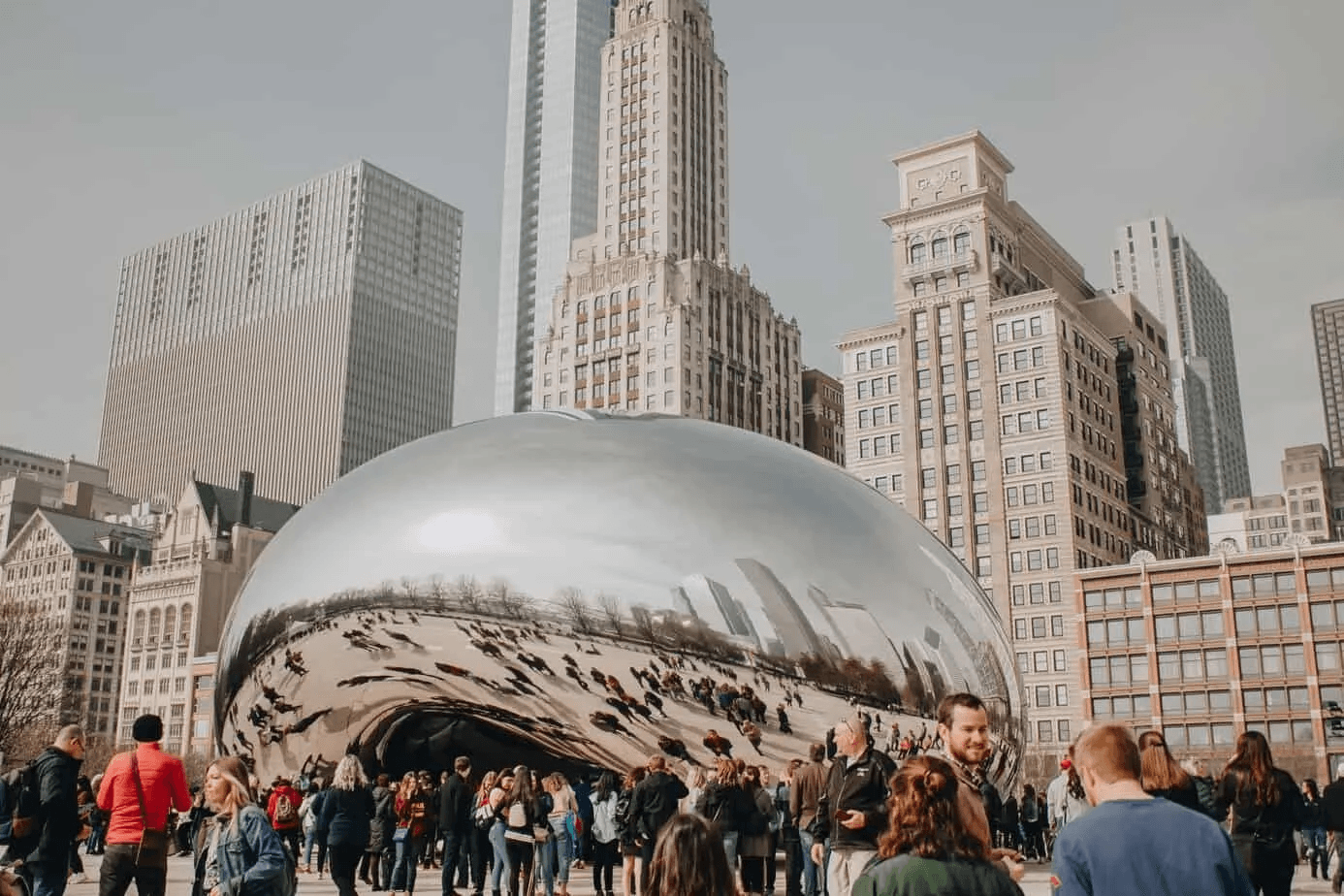 Crowds of tourists gathered around Chicago's reflective Cloud Gate sculpture with skyscrapers behind it