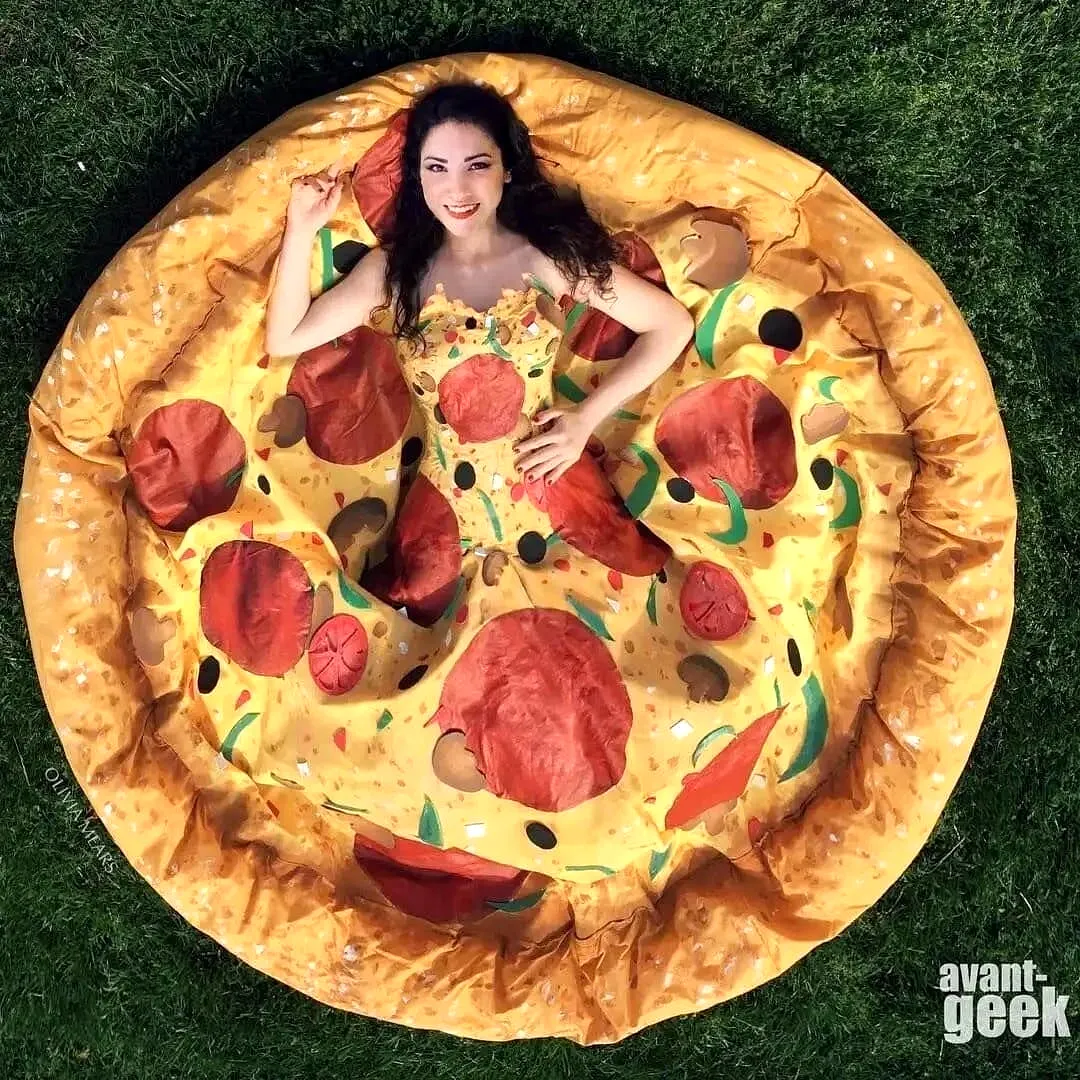 Woman wearing a pizza-themed gown (“Pizza Gown”) lying on grass, top view.