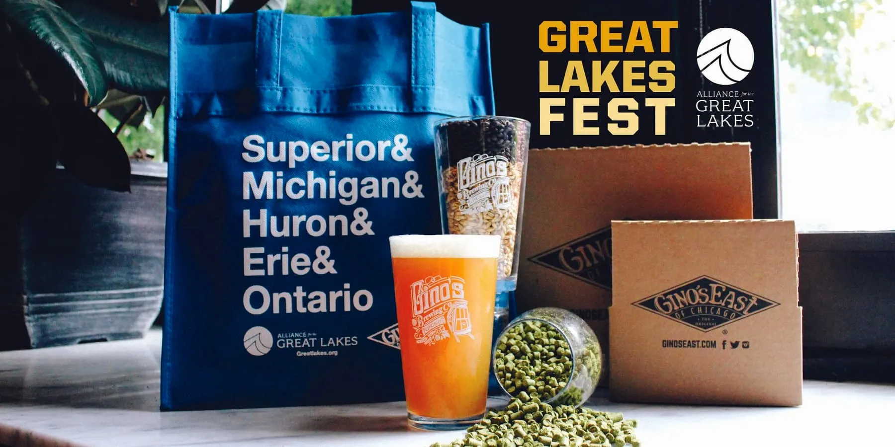 Gino’s East beer glass with hops, branded boxes, and Great Lakes Fest tote bag on a table.