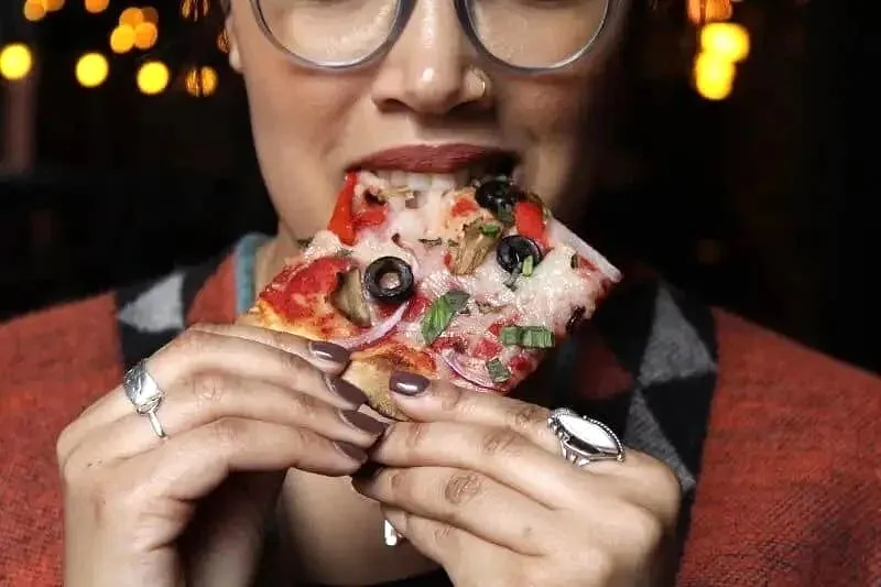 Person eating pepperoni and olive pizza slice with glasses and Christmas lights
