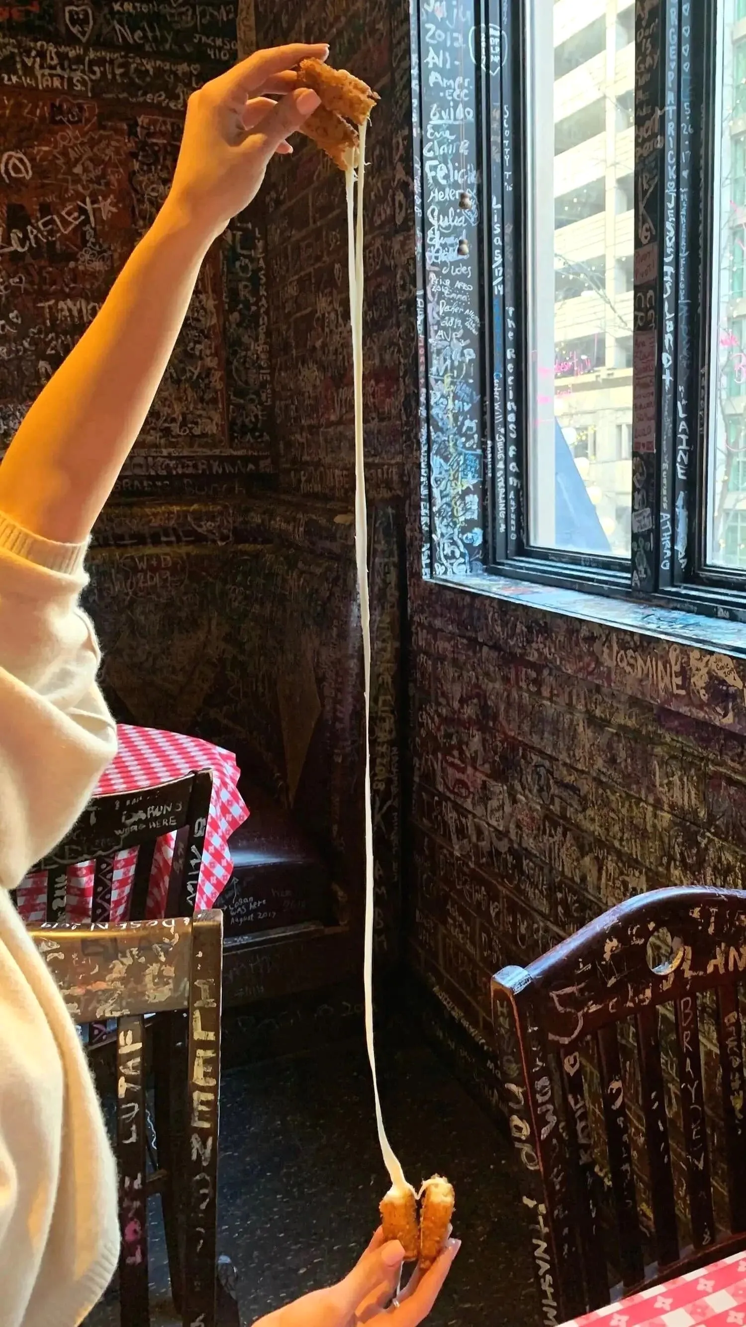 Hand pulling melted cheese from a fried cheese stick in a restaurant interior