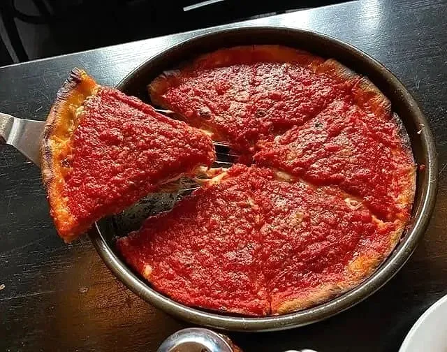 Deep-dish pizza slice being lifted from a black pan with a stretchy cheese pull