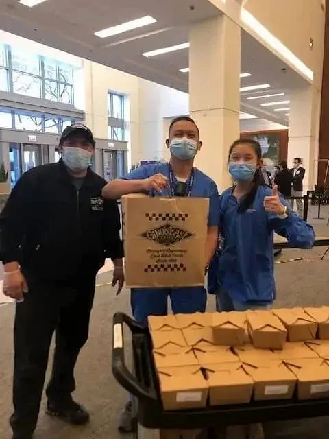 Three people in blue uniforms holding Gino&#x27;s East branded boxes