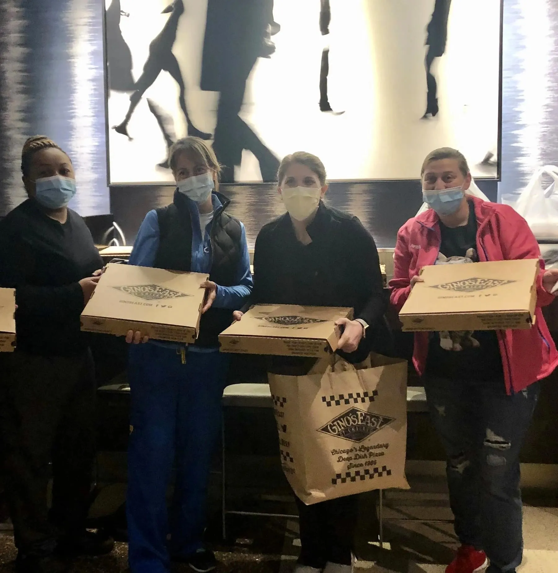 People in winter coats holding Gino&#x27;s East pizza boxes and bag