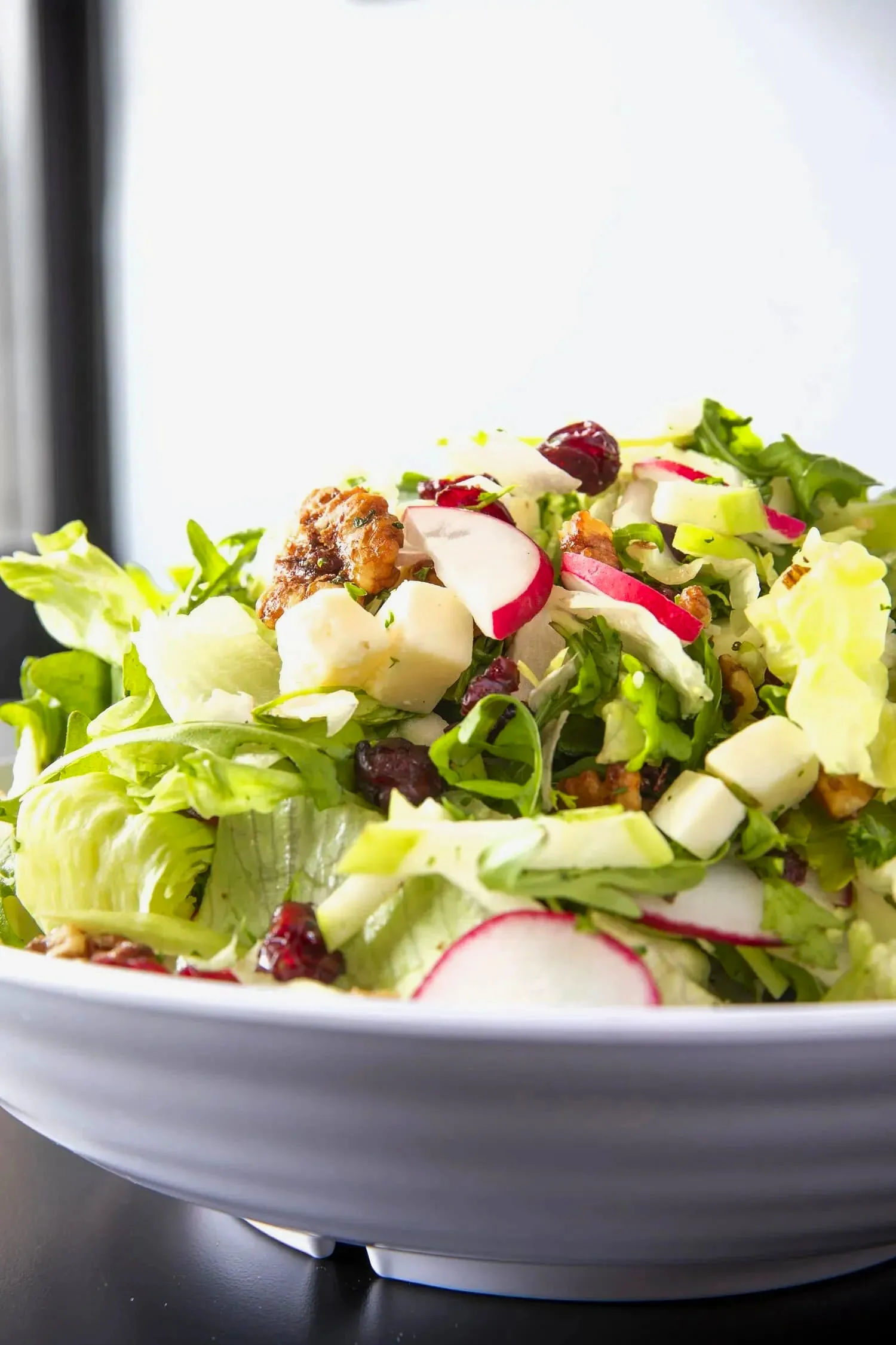 Harvest salad in a white bowl with mixed greens and apple slices topped with walnuts and dried cranberries