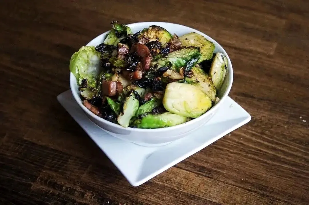Bowl of roasted Brussels sprouts with pancetta and garlic on a wooden table