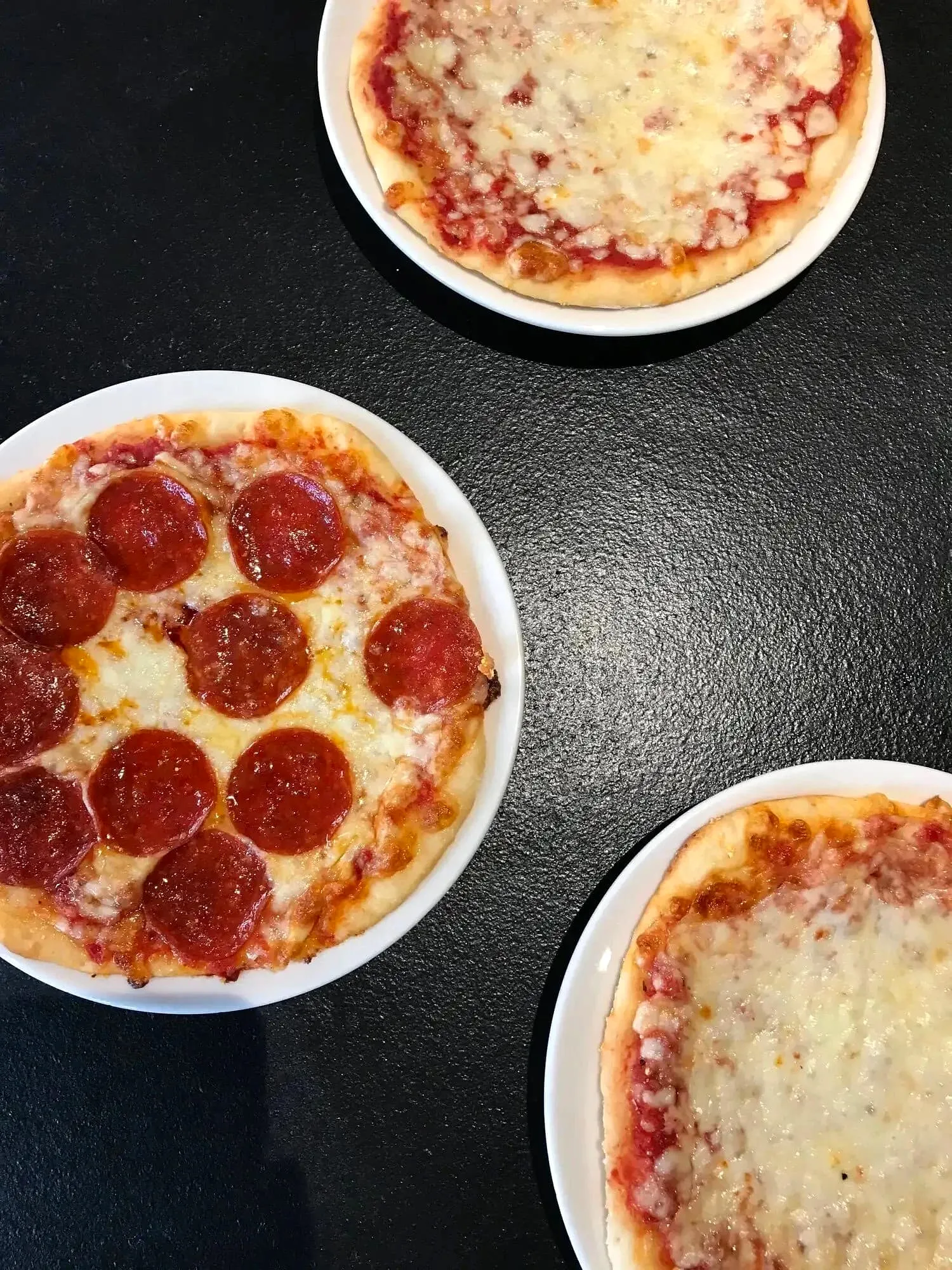 Three small round pizzas with pepperoni and cheese toppings on white plates