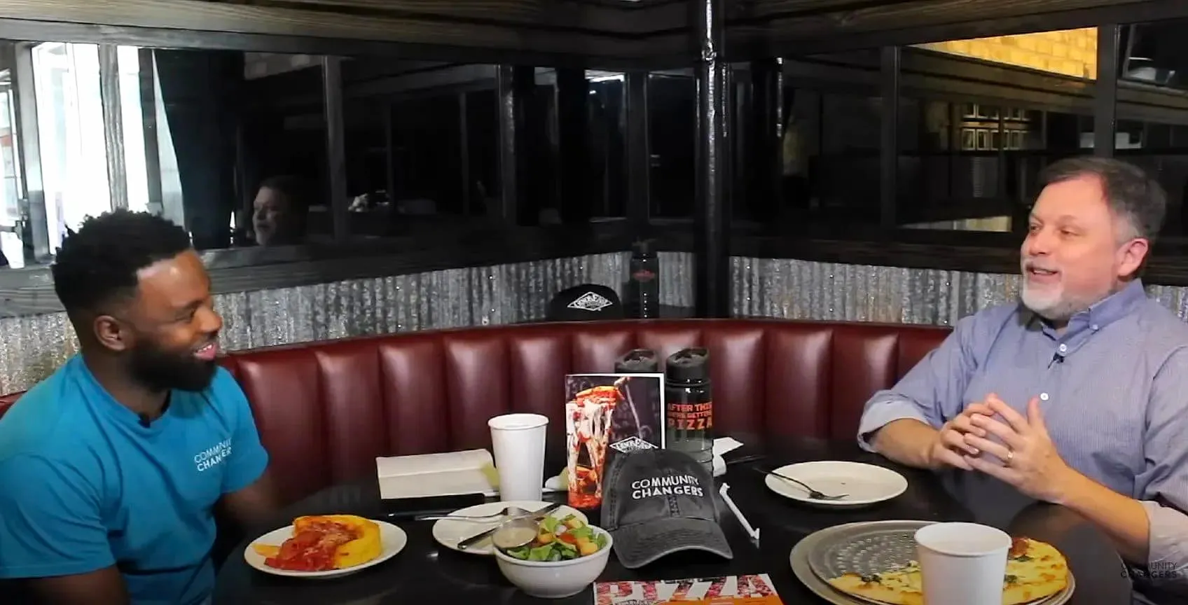 Jerome Moore talking with author and activist Tim Wise over pizza and salad in a booth