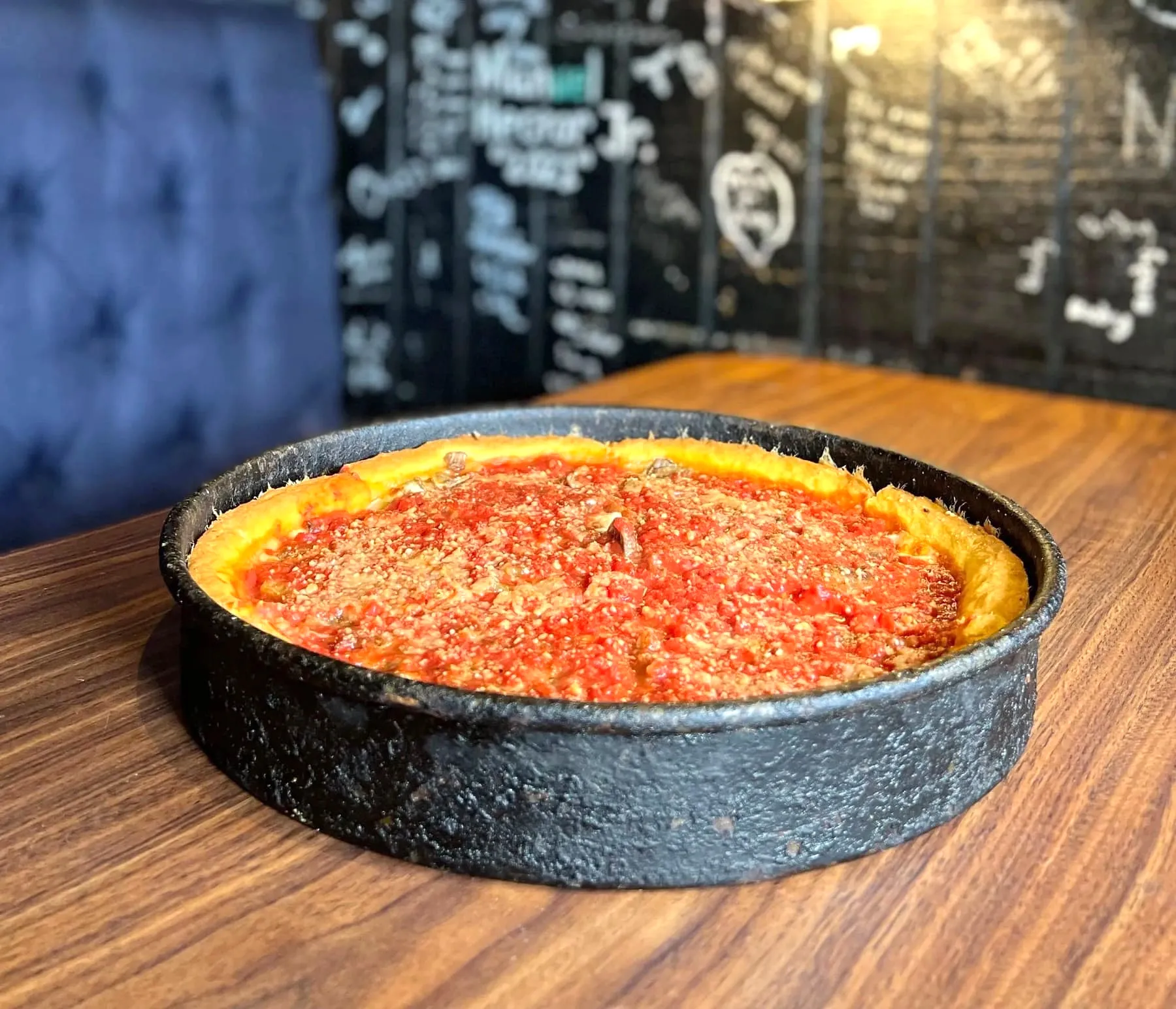 A whole deep dish pizza in its black pan, sauced and topped with parmesan, on a restaurant table