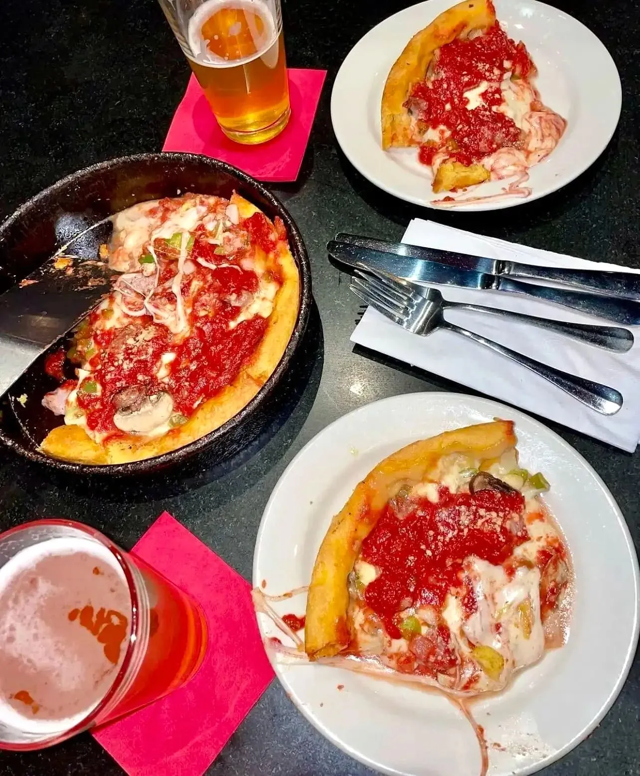 Two plates of deep dish pizza slices next to glasses of beer on a table