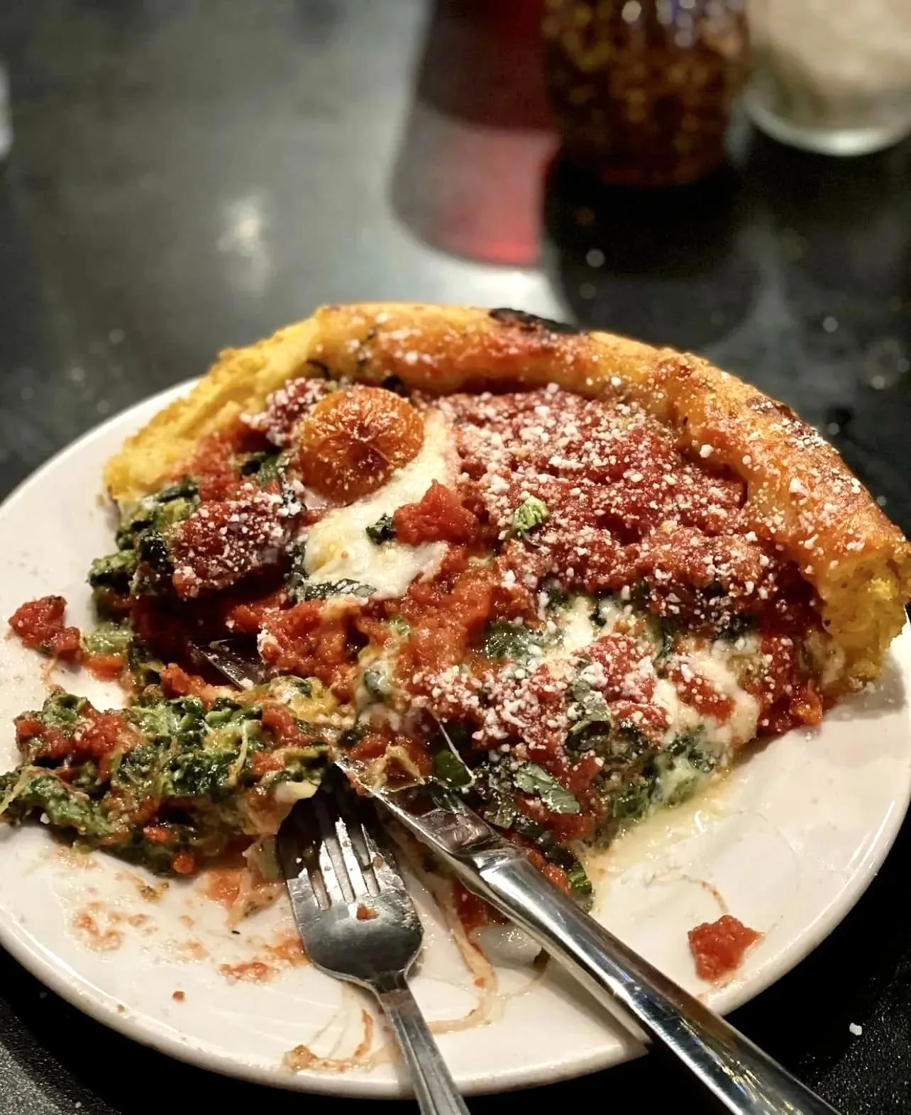 A slice of spinach and tomato deep dish pizza being cut with a fork and knife
