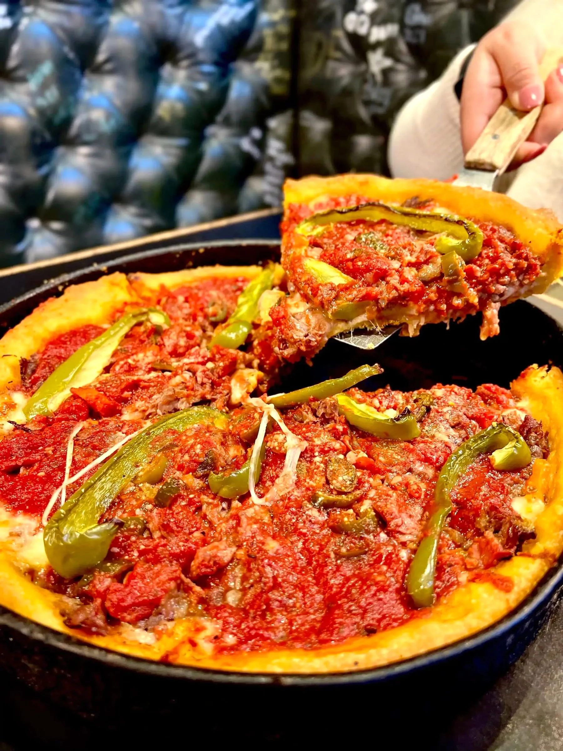 A cheesy slice of deep dish pizza topped with green peppers, lifted from the pan with a spatula