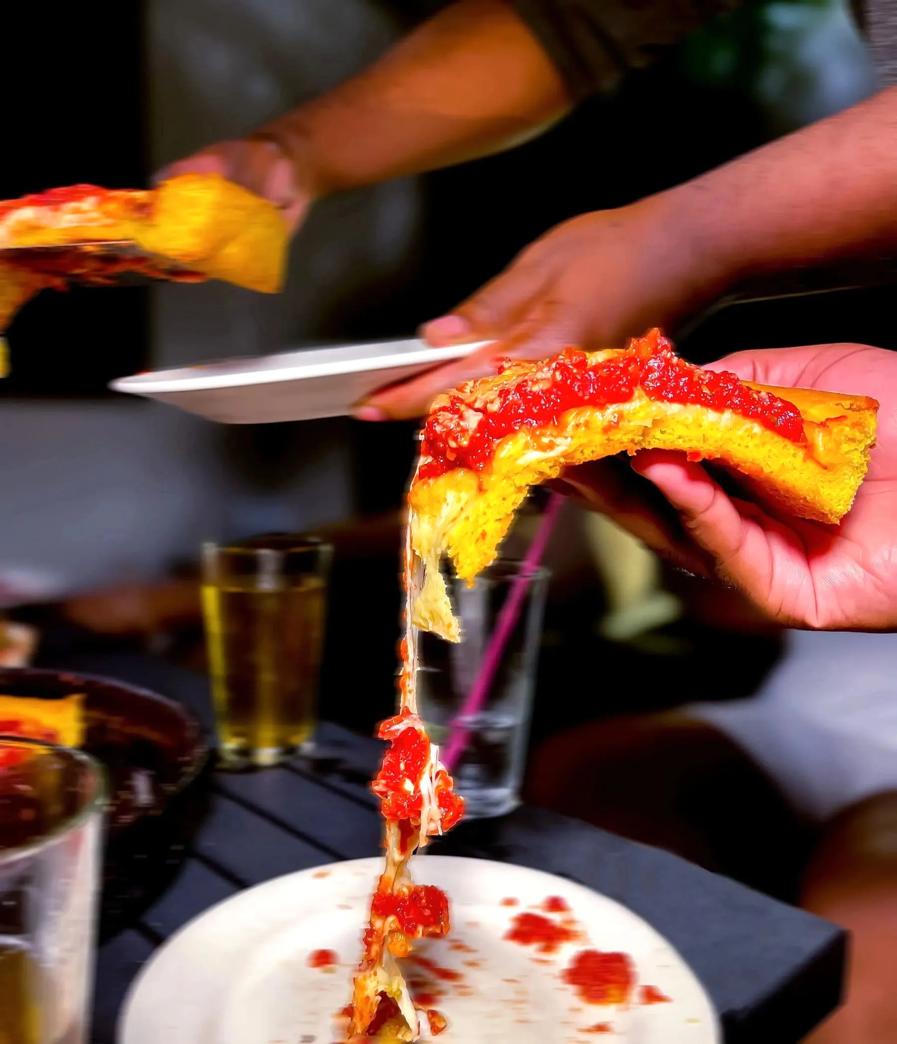 A hand holding up a saucy slice of pizza with melted cheese stretching down to the plate below
