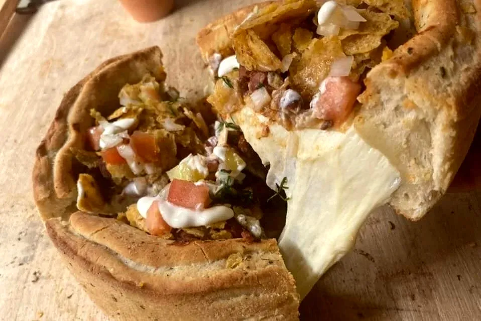 A stuffed pizza pie cut open, revealing beans, diced tomato, sour cream and crispy plantain chips