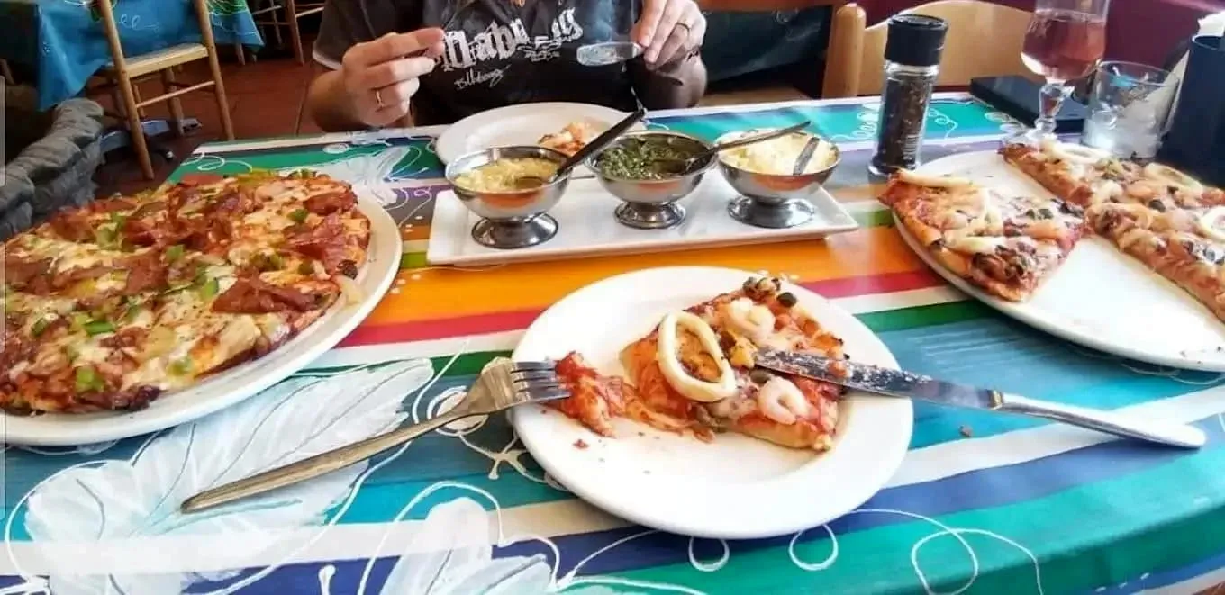 A table of pizzas including a seafood pie topped with shrimp and calamari rings