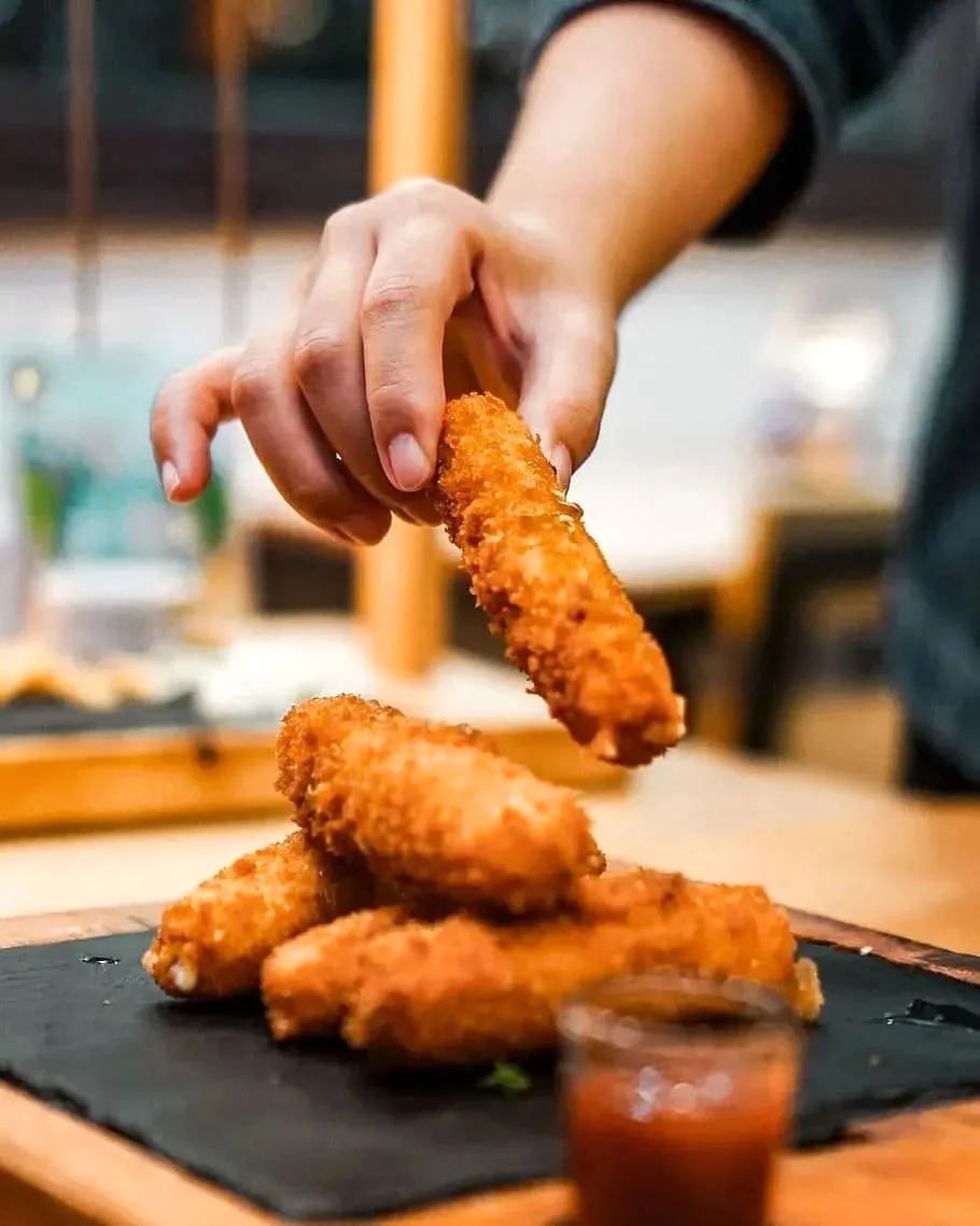 A hand lifting a crispy fried mozzarella stick from a stacked pile with marinara sauce