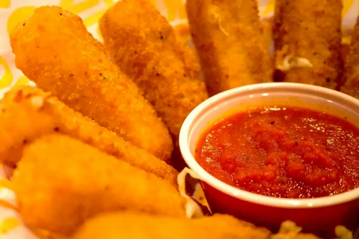 Fried mozzarella sticks arranged around a cup of marinara dipping sauce