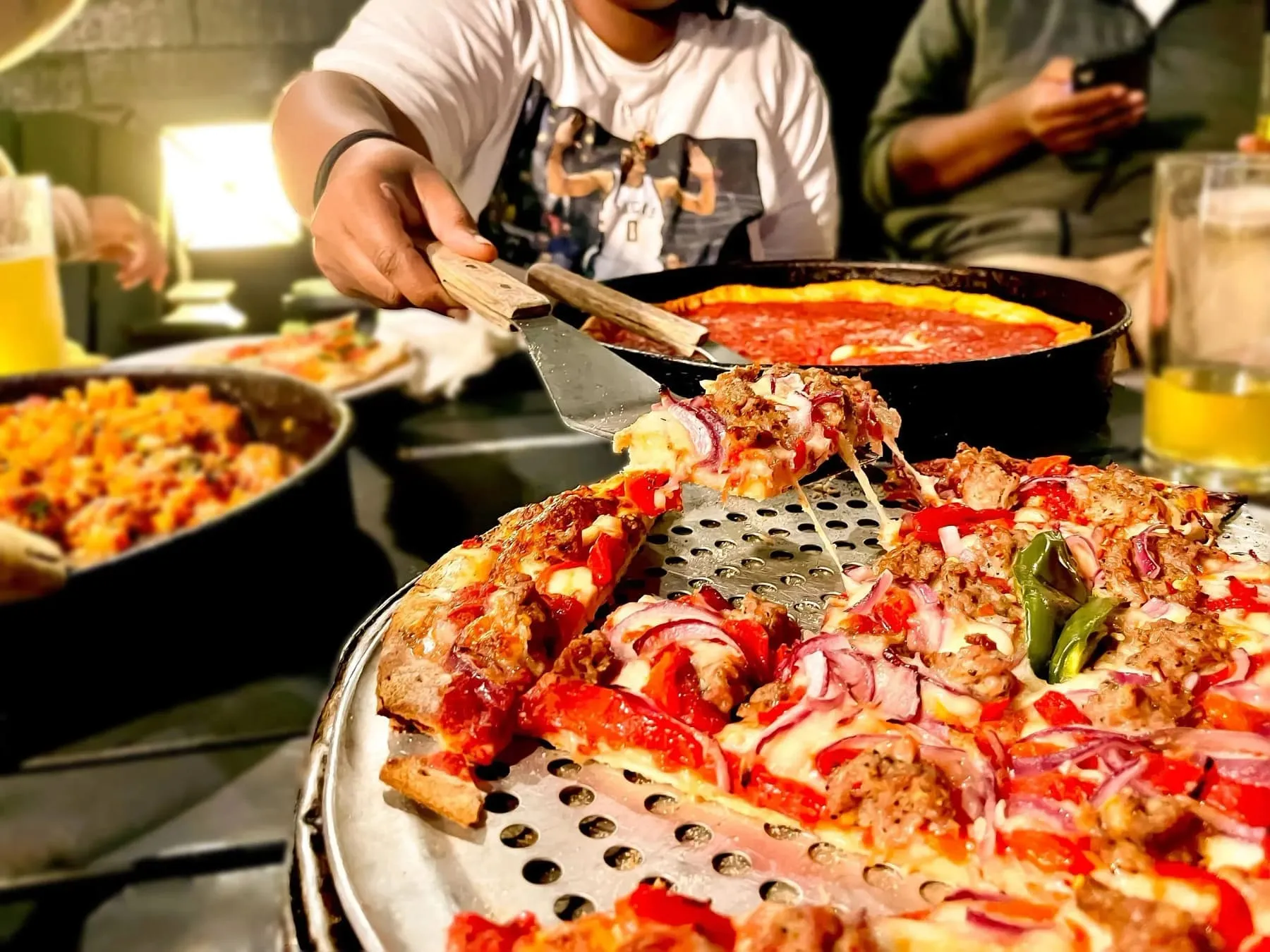 A stretchy cheese slice of deep dish pizza loaded with sausage, peppers, and onions being lifted from the pan