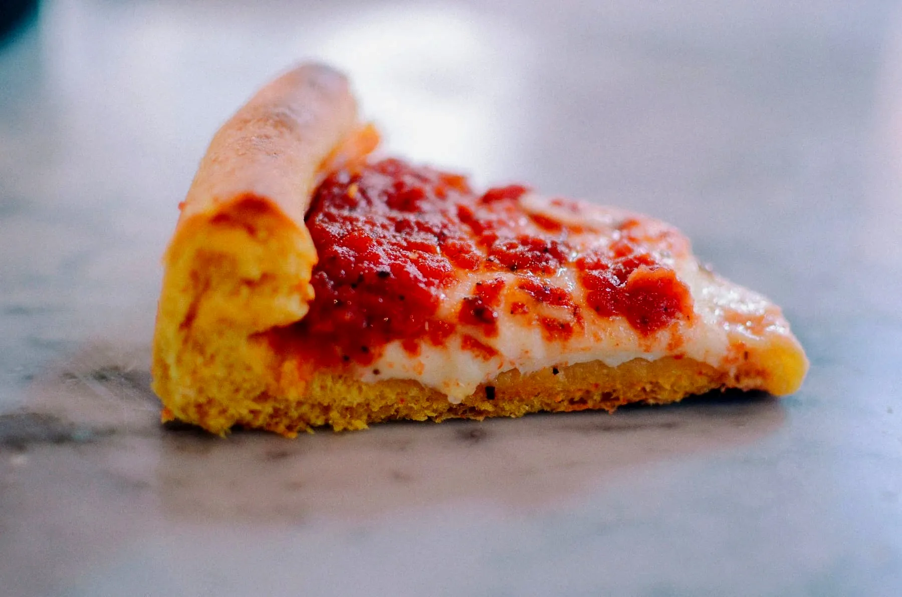 A close-up side view of a cheesy deep dish slice on a marble counter