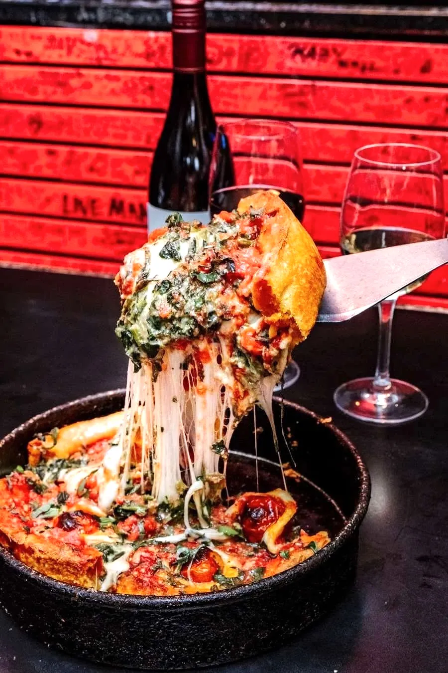 A slice of spinach and tomato deep dish pizza lifted from the pan with cheese stretching down