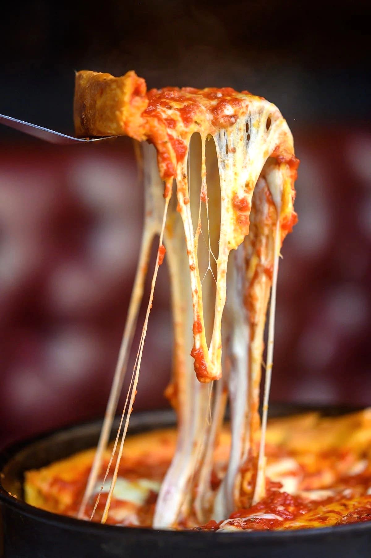 Close-up of a fork lifting a slice of cheesy pepperoni pizza with melted cheese stretching.