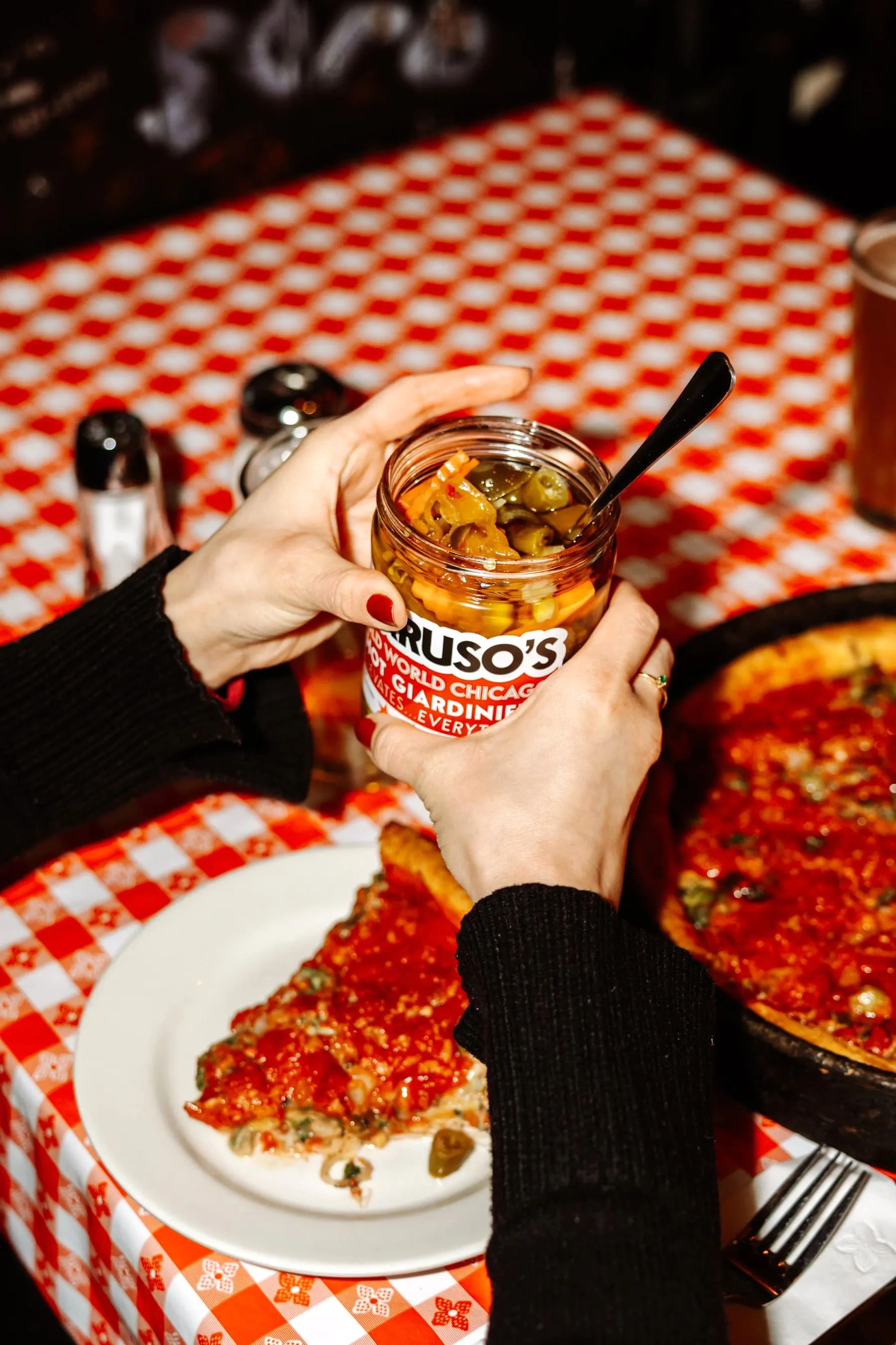 A slice of spinach and tomato deep dish pizza lifted with a cheesy stretch, wine glasses in the background