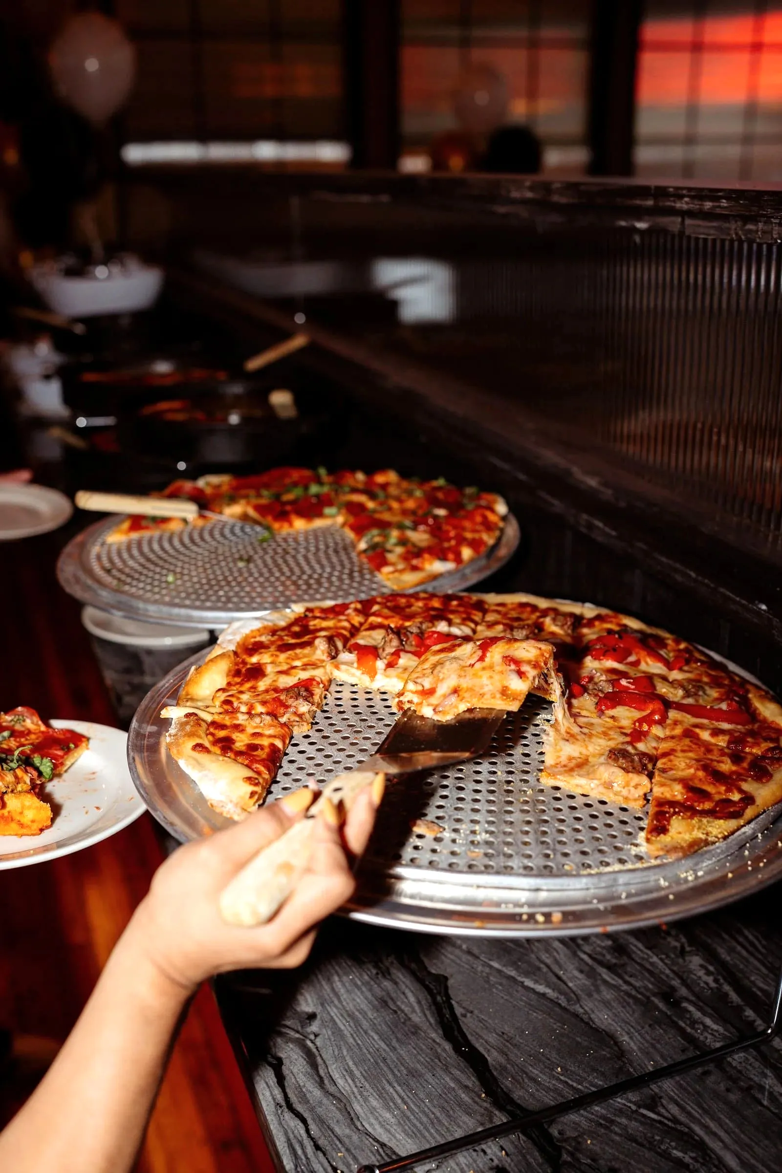 A hand pulling a slice of sausage and pepper pizza from a tray at a pizza counter