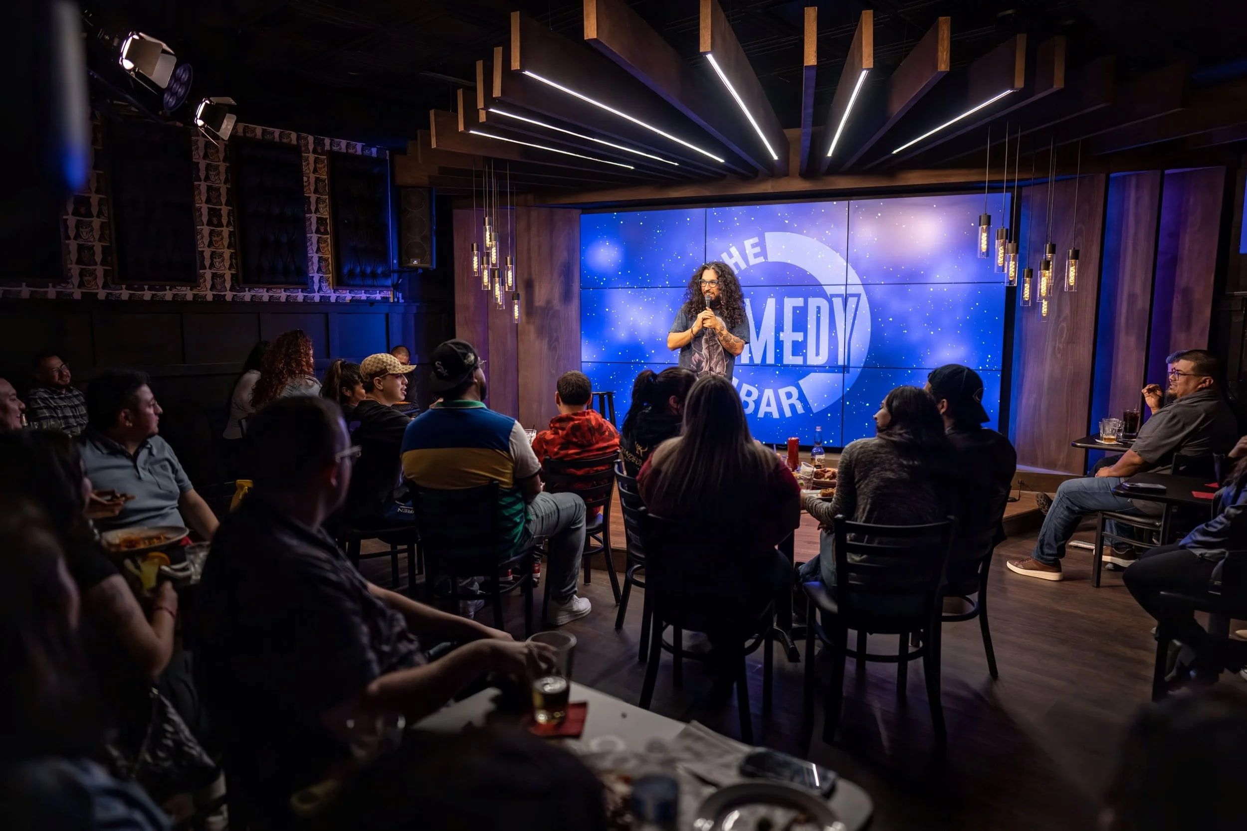 A comedian performing on The Comedy Bar stage to a full room of guests at tables