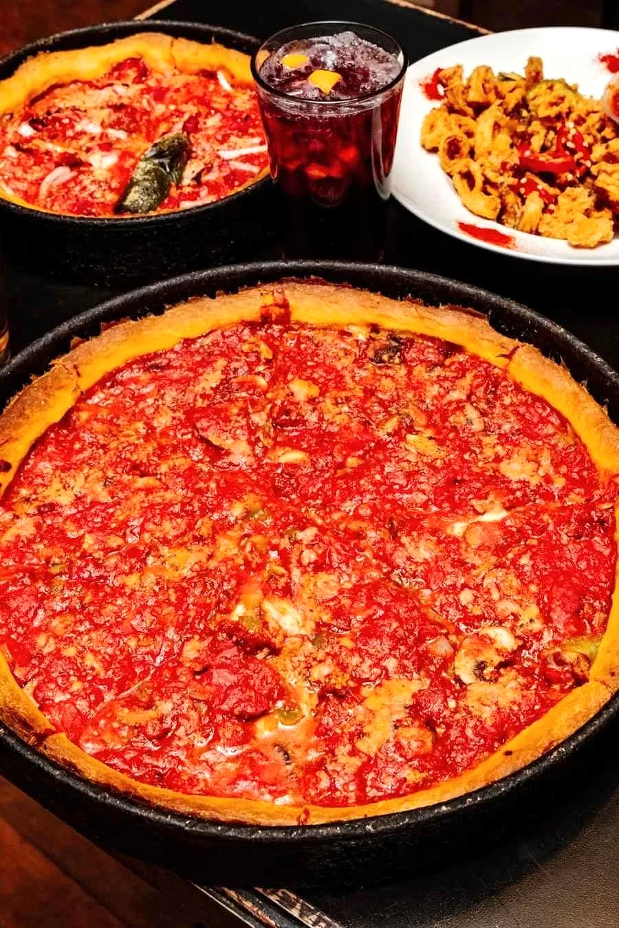 Deep dish pizzas with thick chunky tomato sauce toppings served alongside fried calamari and drinks