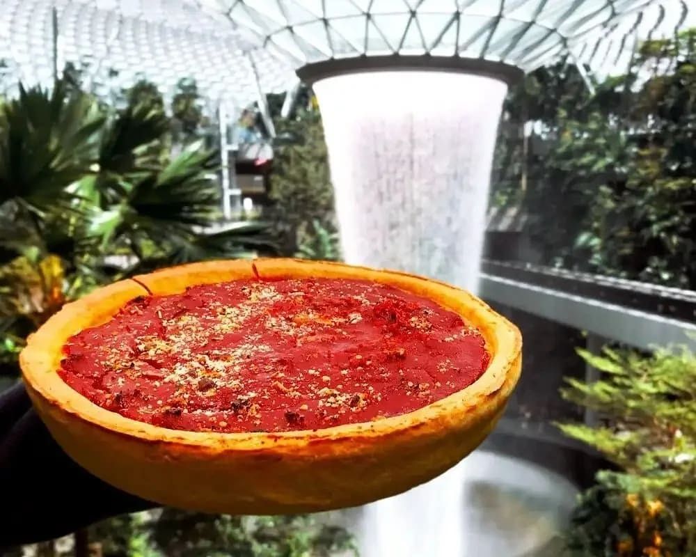 A Gino's East deep dish pizza in front of the Jewel Changi Airport indoor waterfall in Singapore