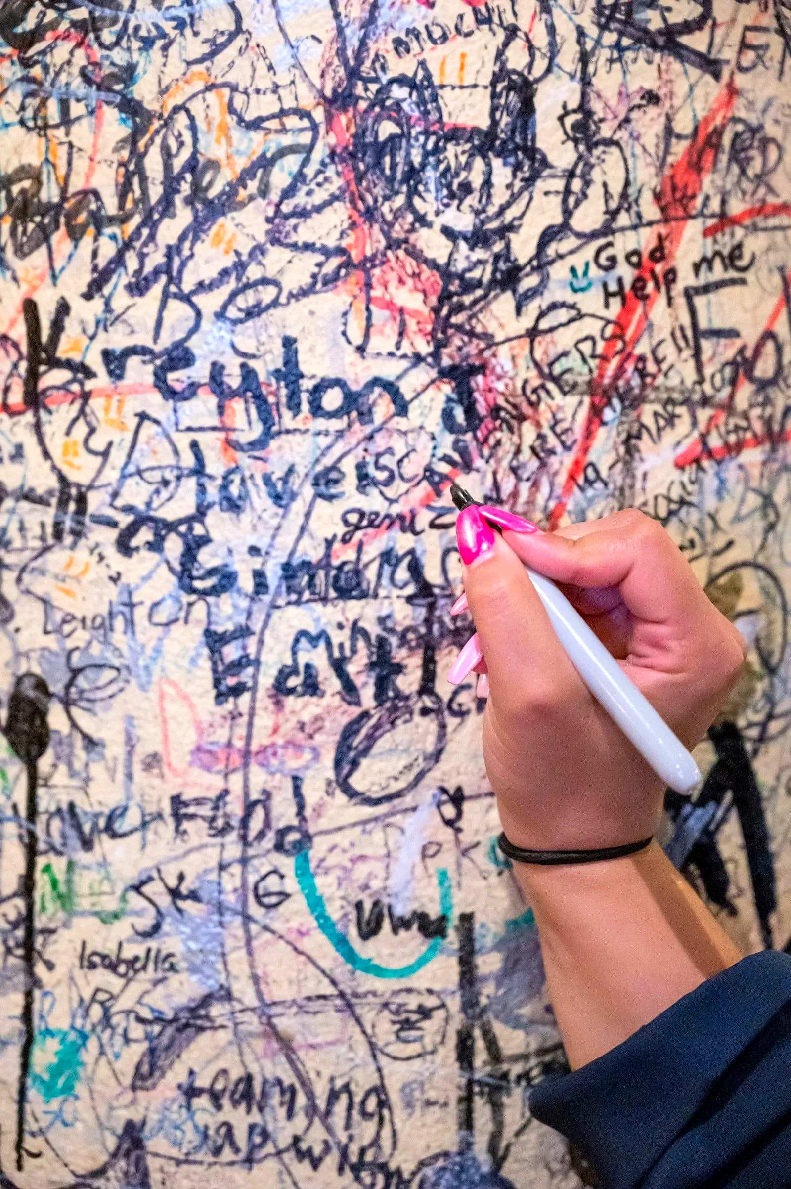 Close-up of a hand adding a signature in marker among dense layers of wall graffiti