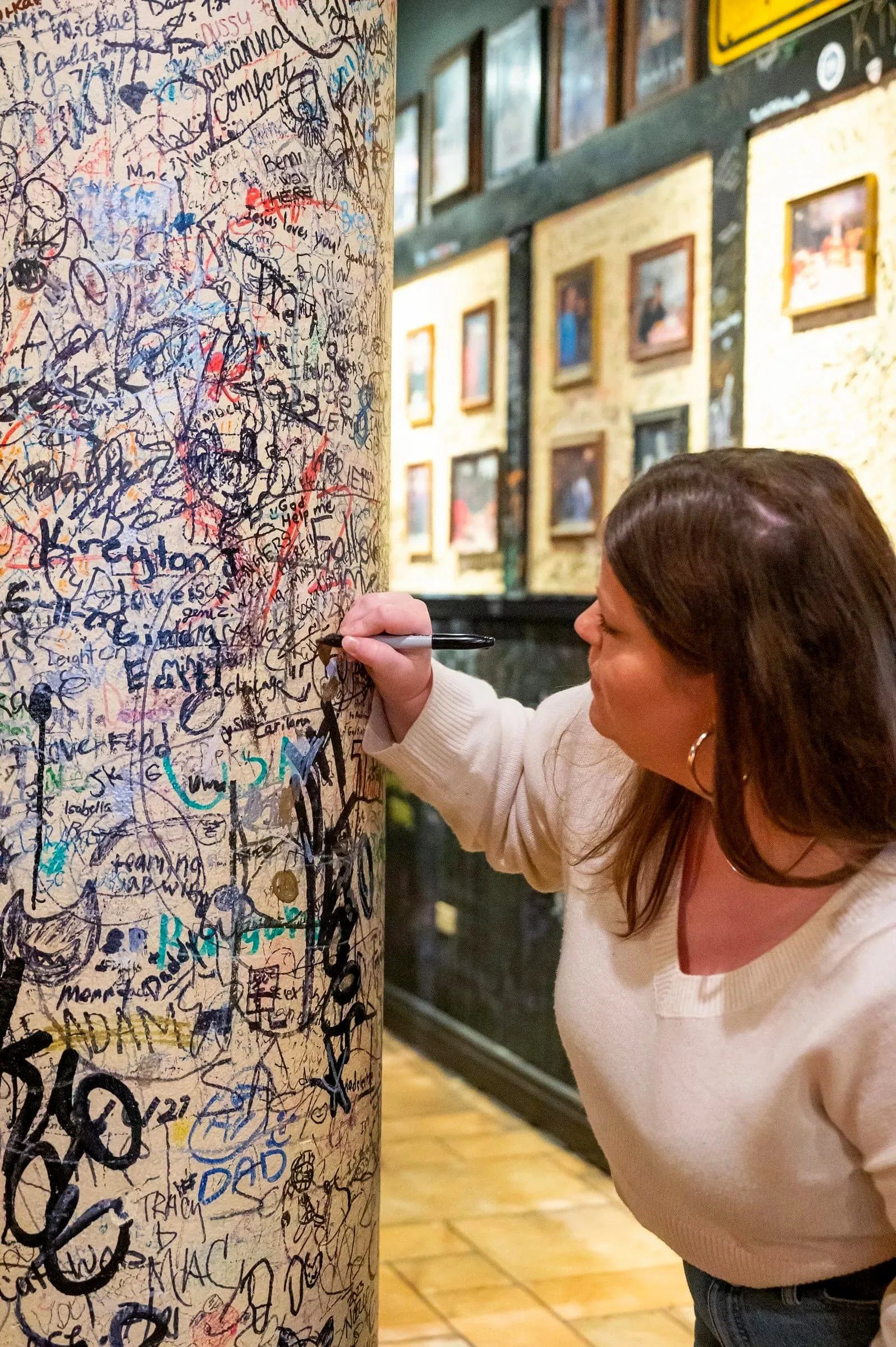 A woman signing her name on a marker-covered column among thousands of visitor signatures