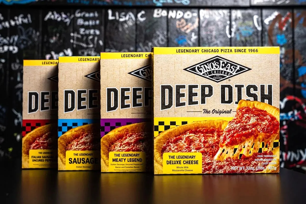 Four Gino’s East frozen deep dish pizza box varieties lined up in front of the signature graffiti wall