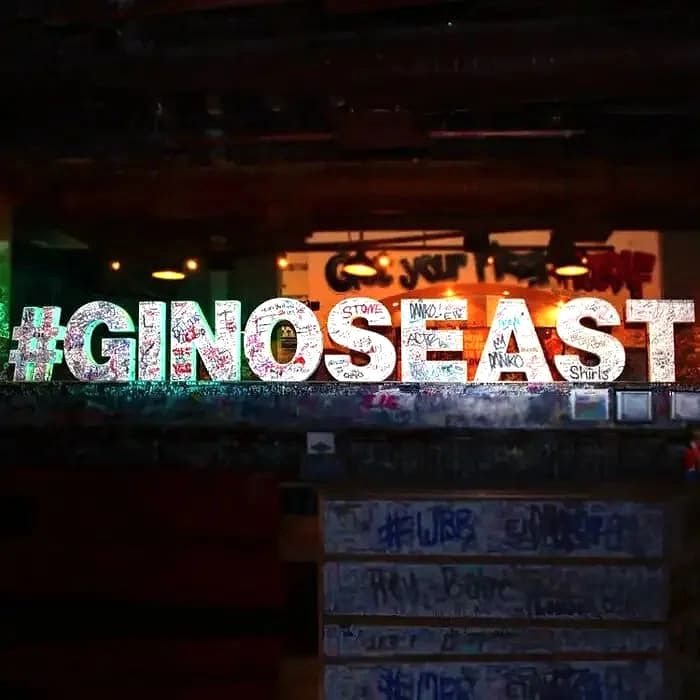 Neon '#GINOSEAST' sign on a graffiti-covered wall