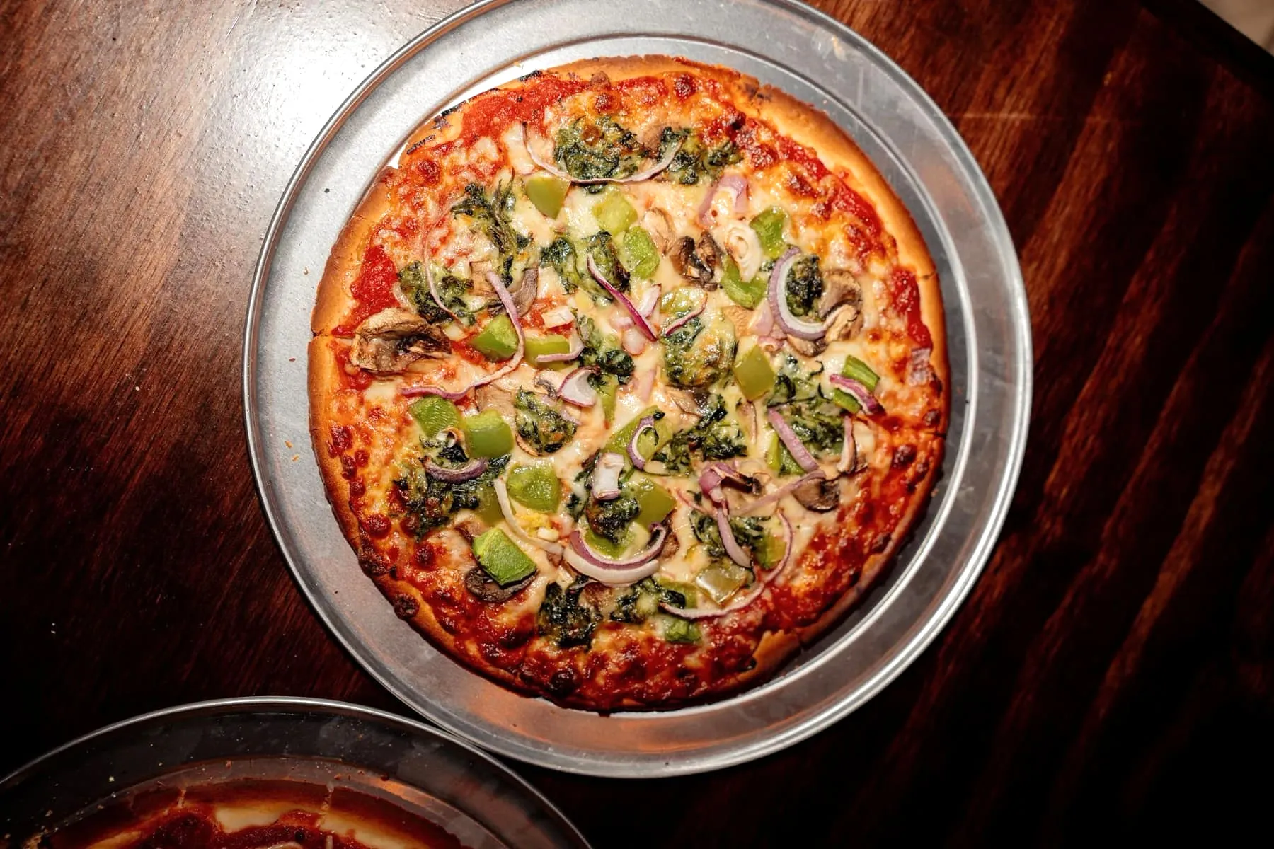 A gluten-free thin crust pizza topped with spinach, green peppers, red onion, and mushrooms