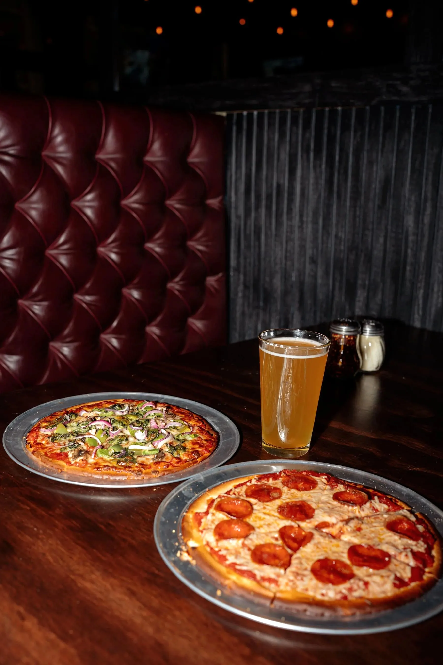 Two gluten-free pizzas, veggie and pepperoni, served on a booth table with a glass of beer