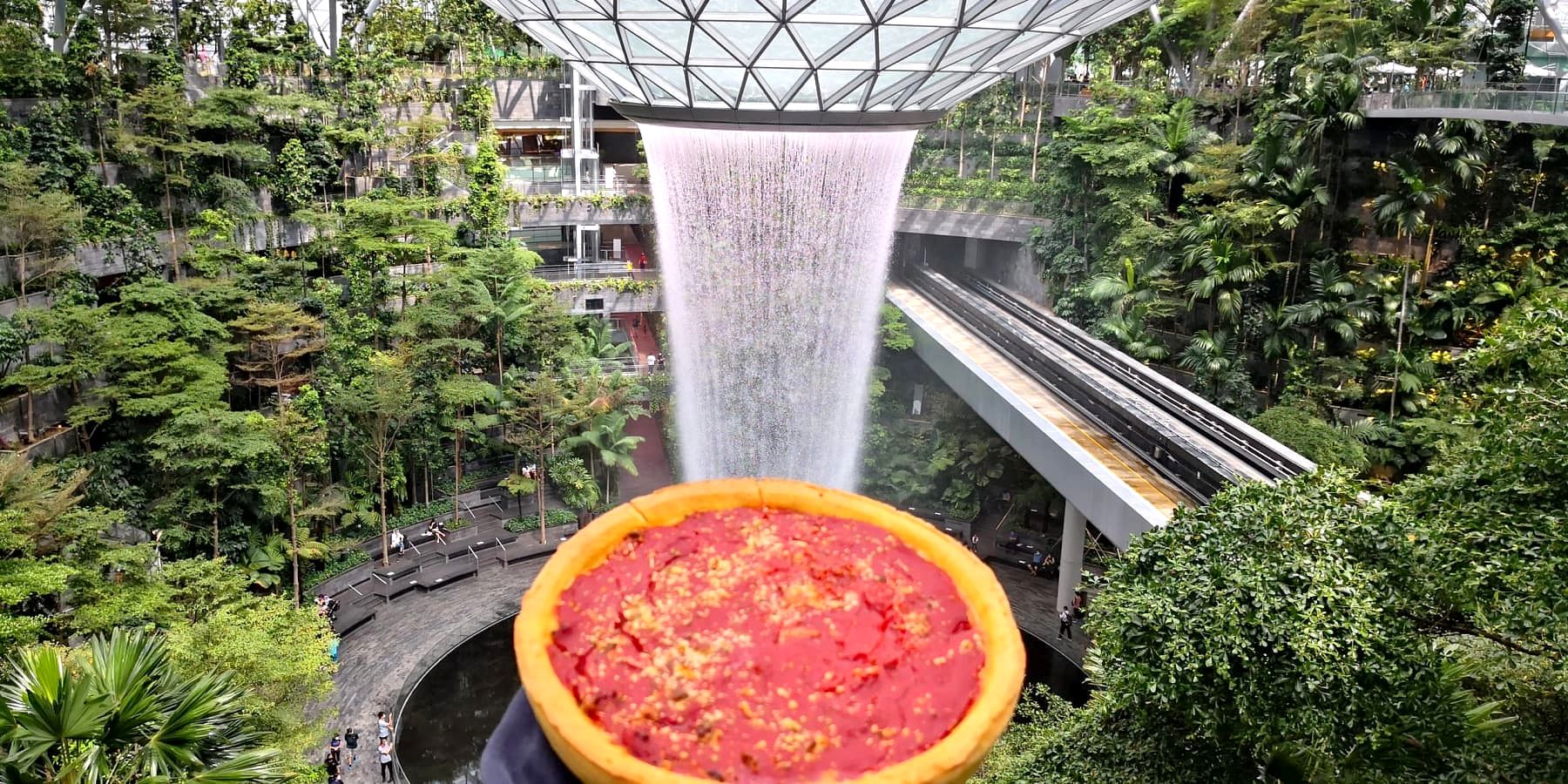 A Gino's East deep dish pizza held up in front of the Jewel Changi Airport waterfall in Singapore