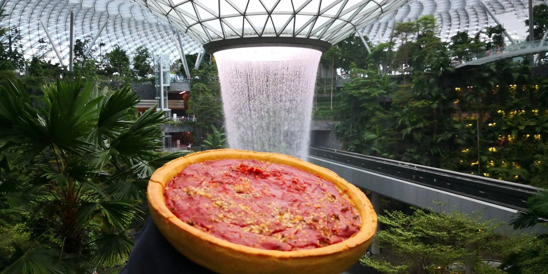 Pepperoni pizza at Jewel Changi Airport's indoor waterfall, with lush greenery and a glass roof