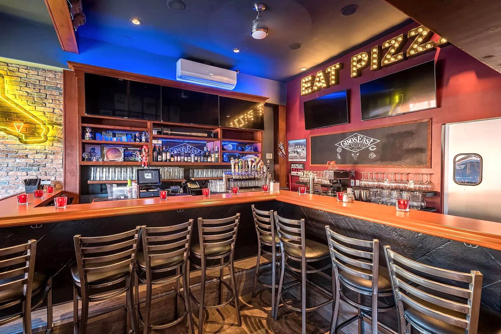 Interior of the Gino's East LA bar with a wooden counter, barstools, and an 'EAT PIZZA' marquee sign