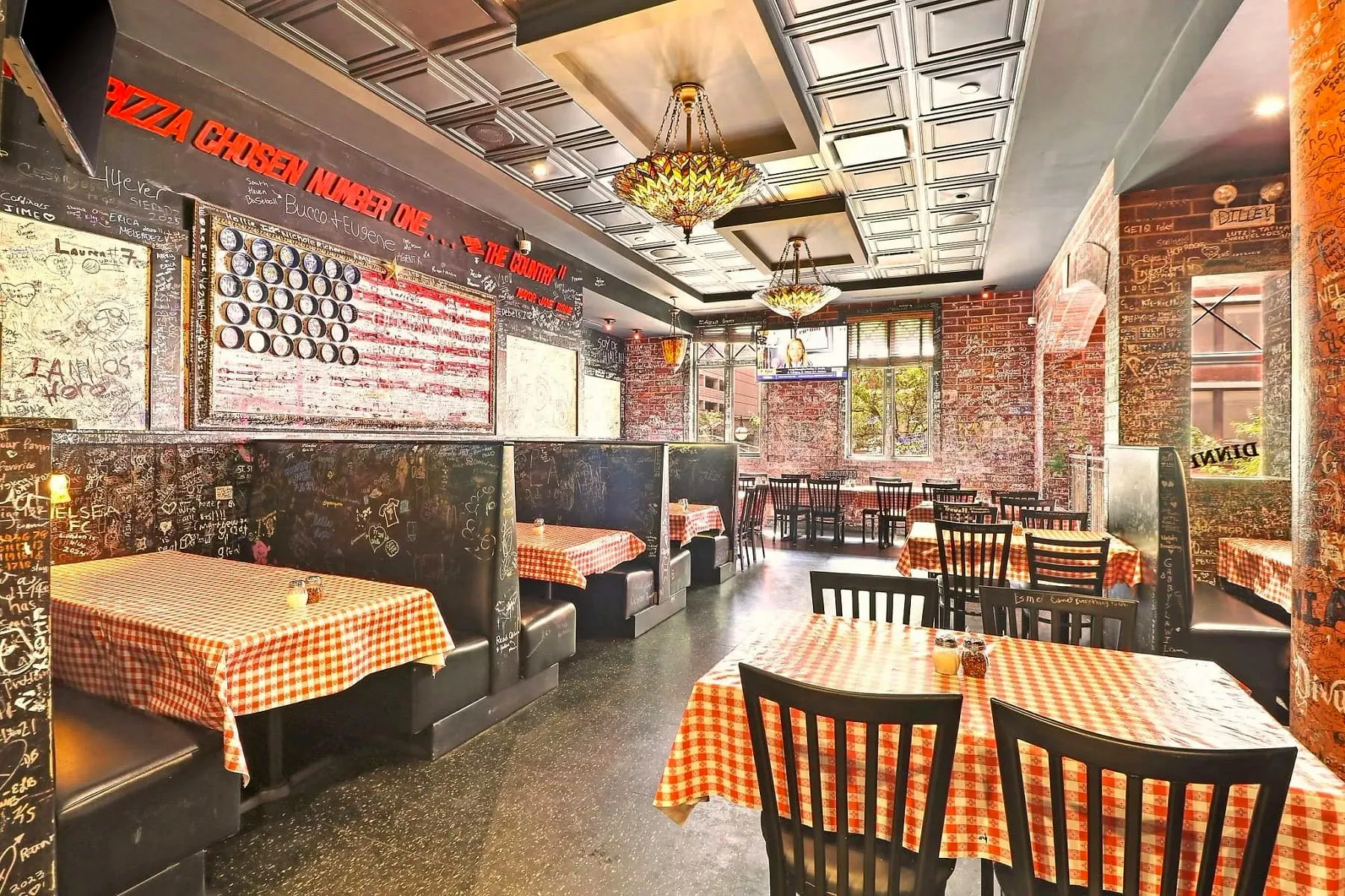 Graffiti-covered dining room at Gino’s East Magnificent Mile, red-checkered tablecloths and booths under signatures in chalk and marker