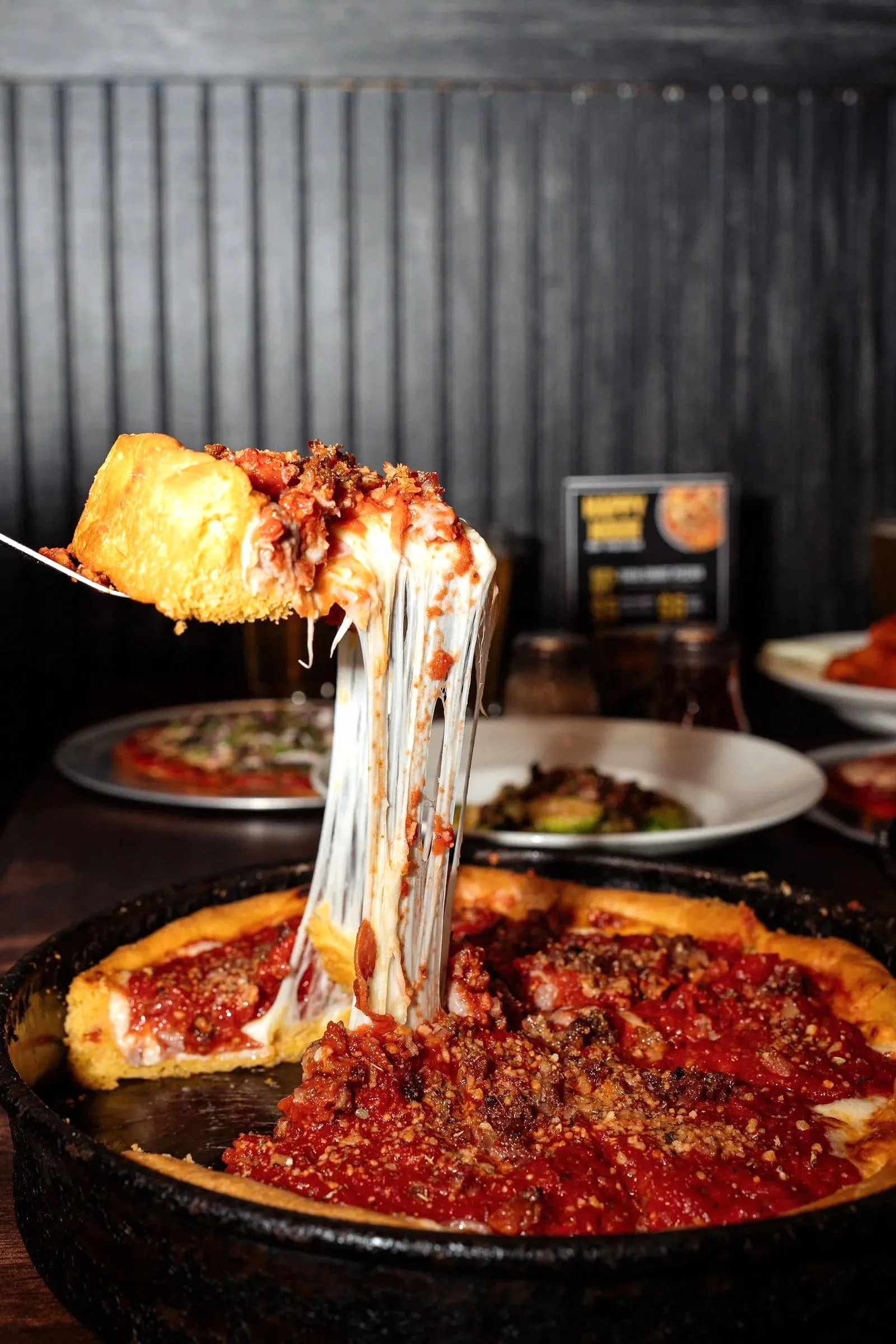 Cheese pull as a slice of Chicago deep dish pizza topped with sausage and beef is lifted from the pan